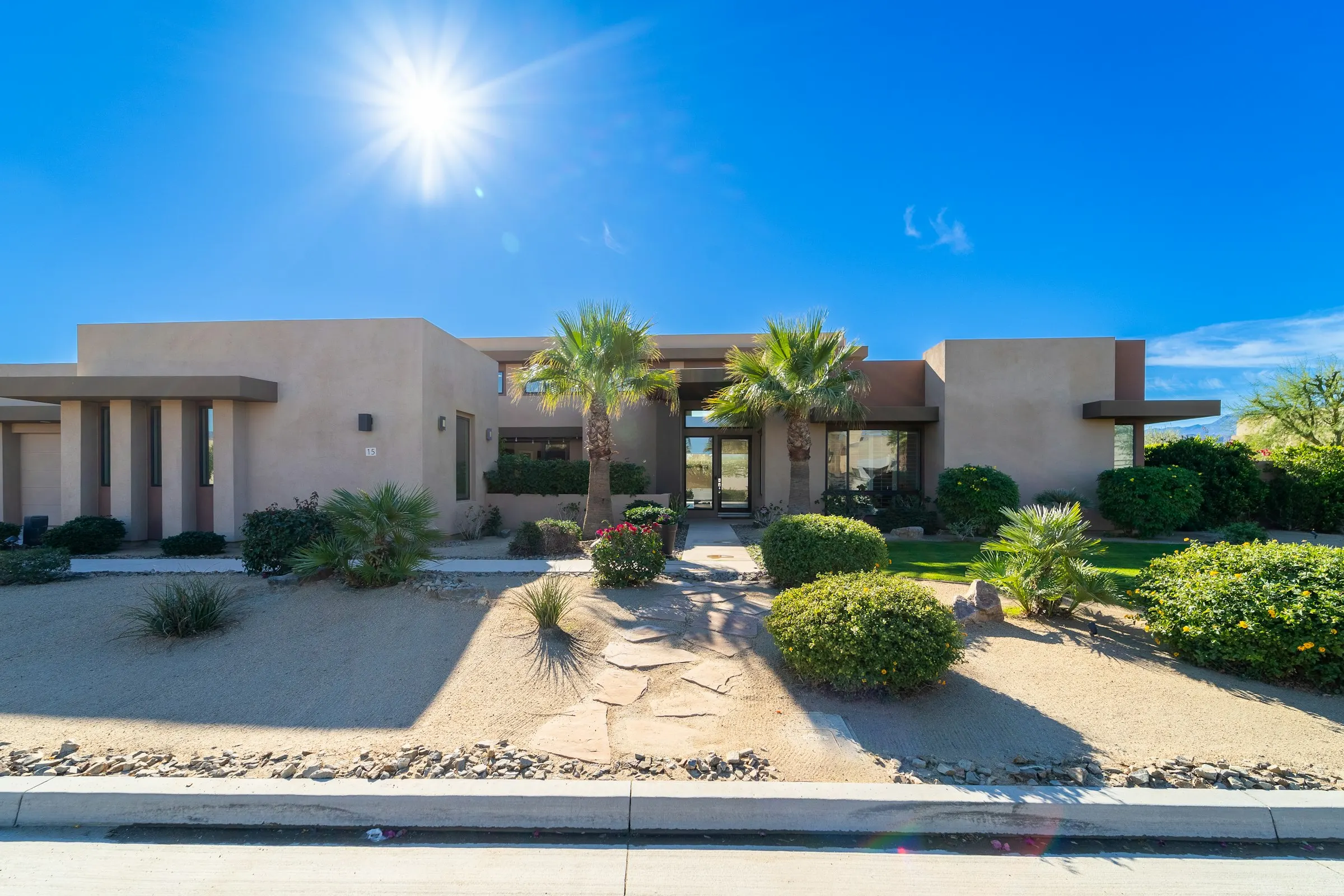 Desert-style front yard with palms, clipped shrubs, and decomposed granite under a bright sun