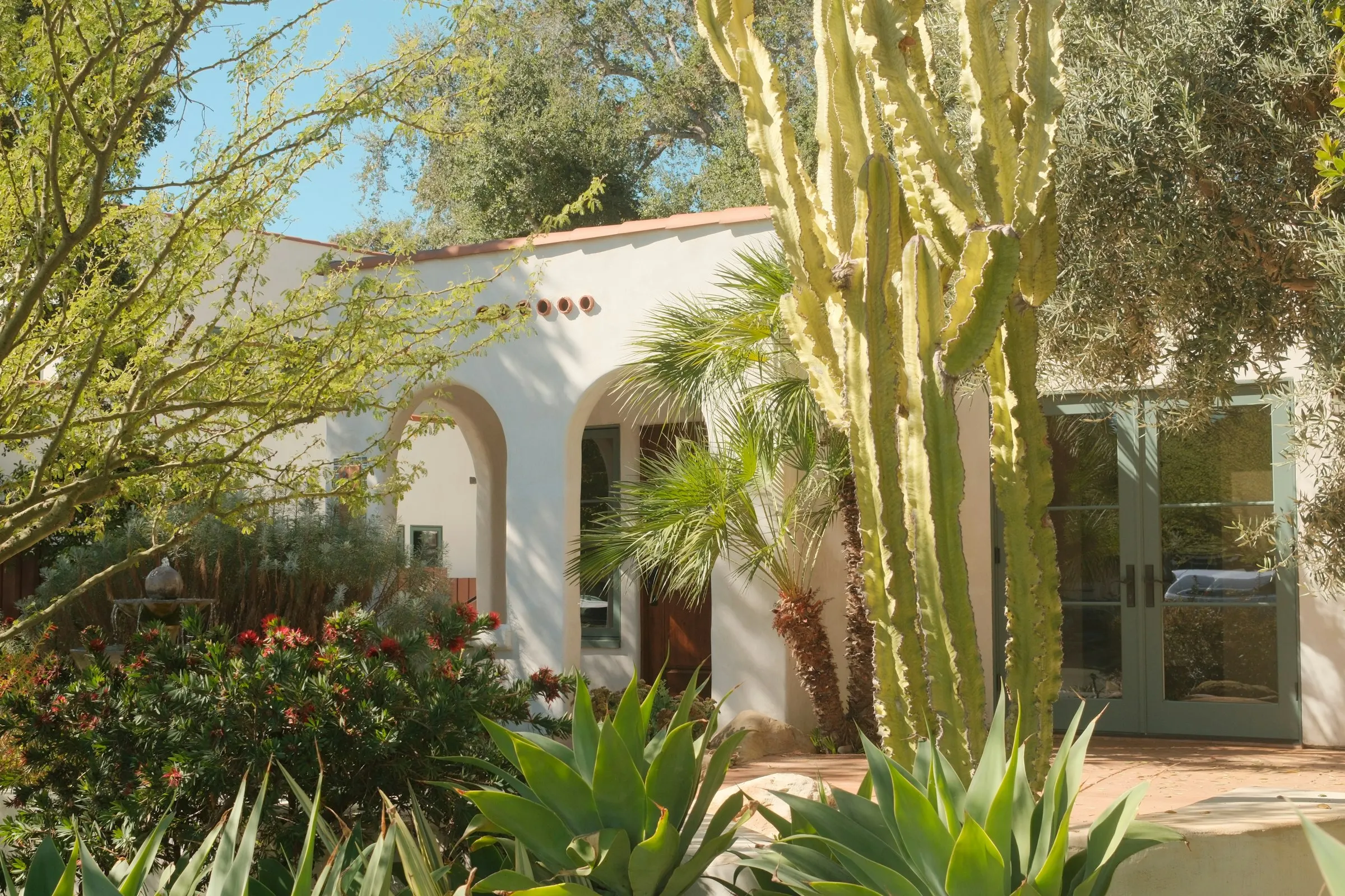 Spanish-style home entry framed by cactus, agave, and flowering desert plants