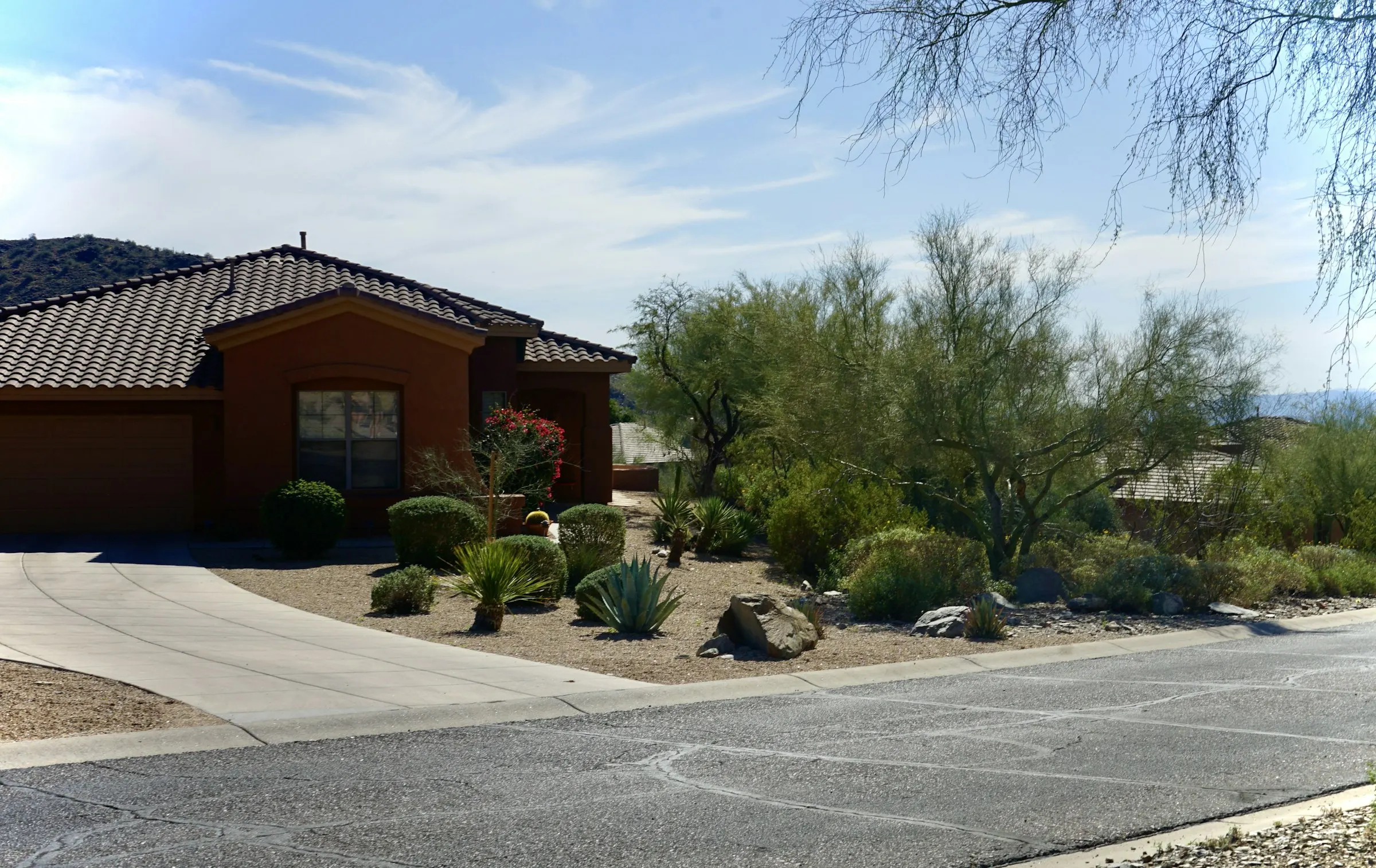 Tile-roof home with a desert-landscaped front yard of shrubs, boulders, and small trees